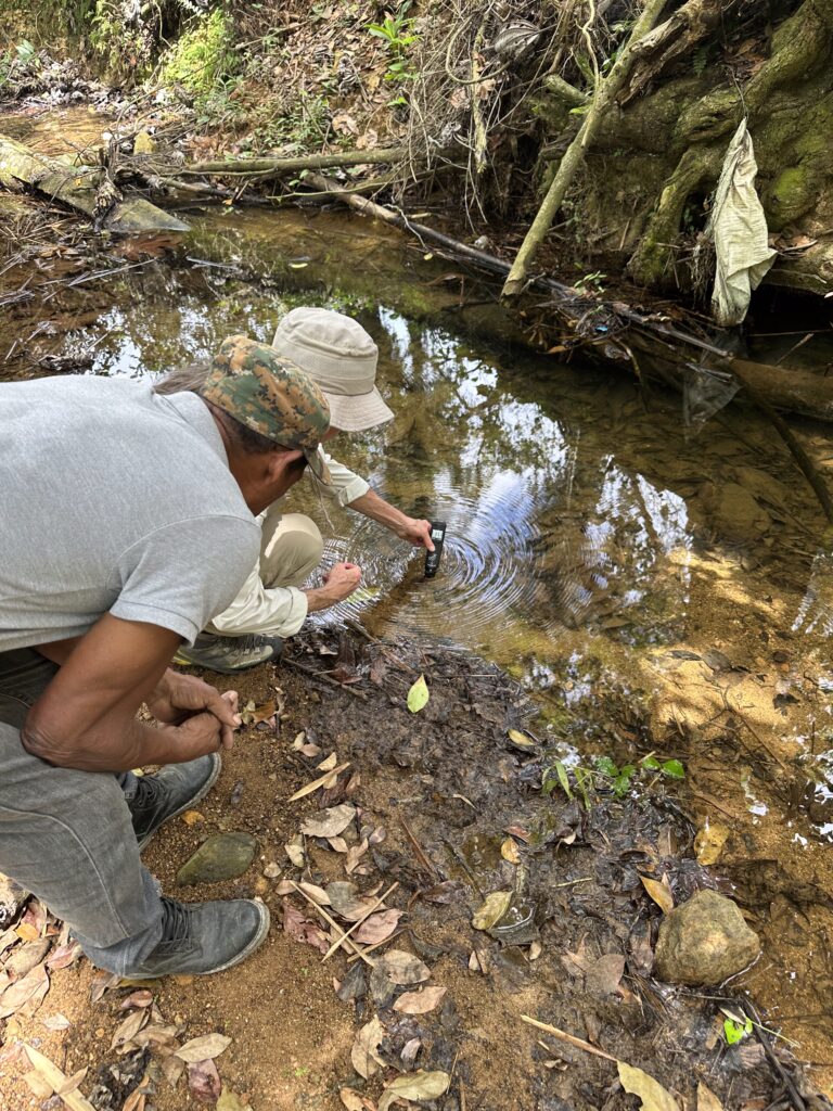 Two people lean over a stream with hand-held testing equipment