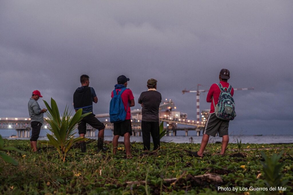 five people look across water at lights of an industrial port