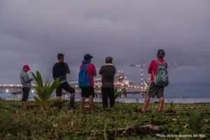 five people look across water at lights of an industrial port