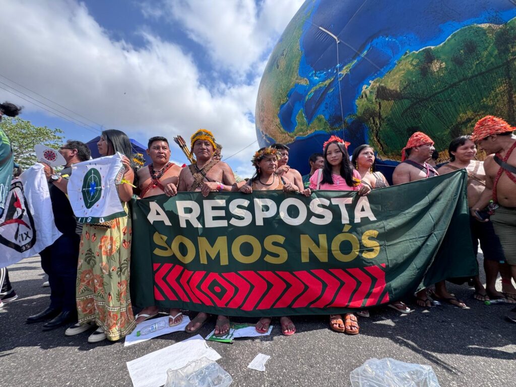 Indigenous People with a banner reading "The answer is us" in Portuguese